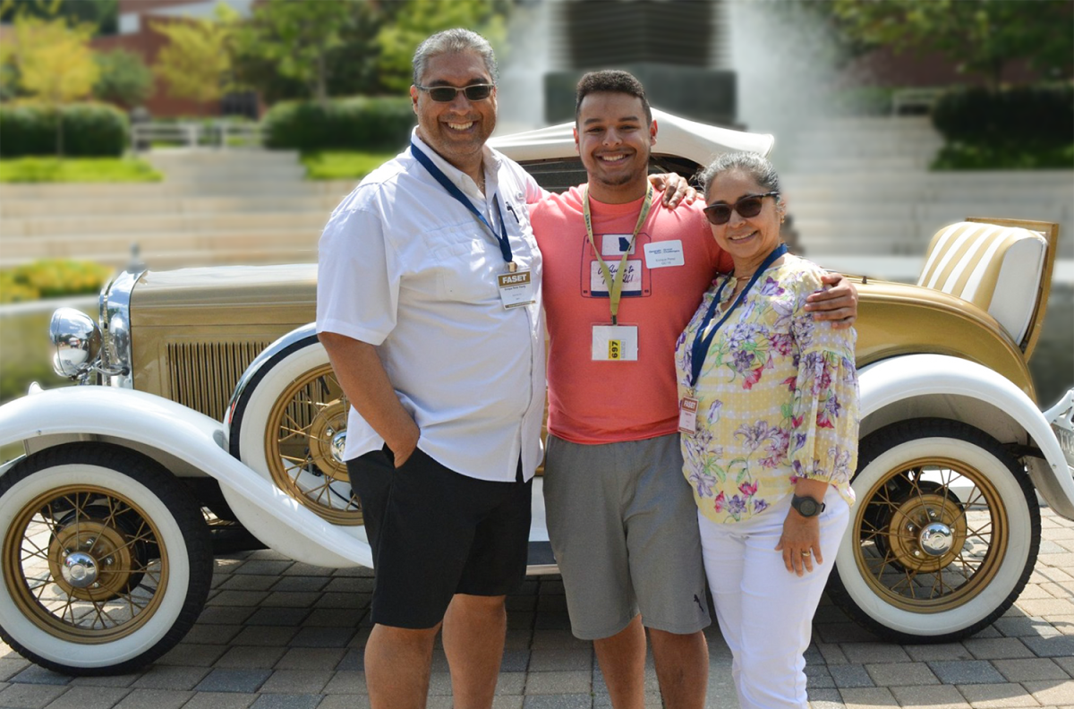 Parents with their son posing in front of the Ramblin' Wreck car.