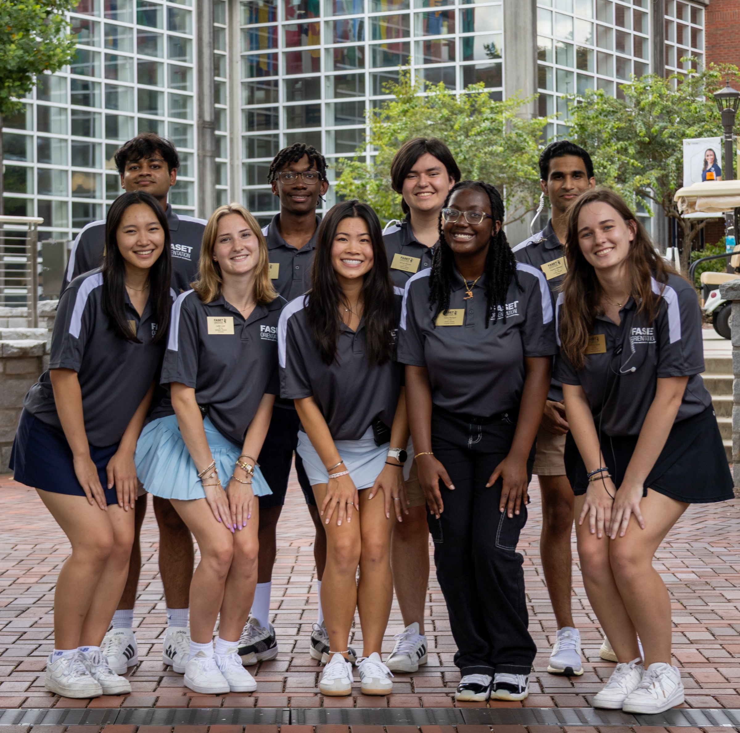 Nine college-age students all wearing identical FASET staff tshirts stand close together and smile
